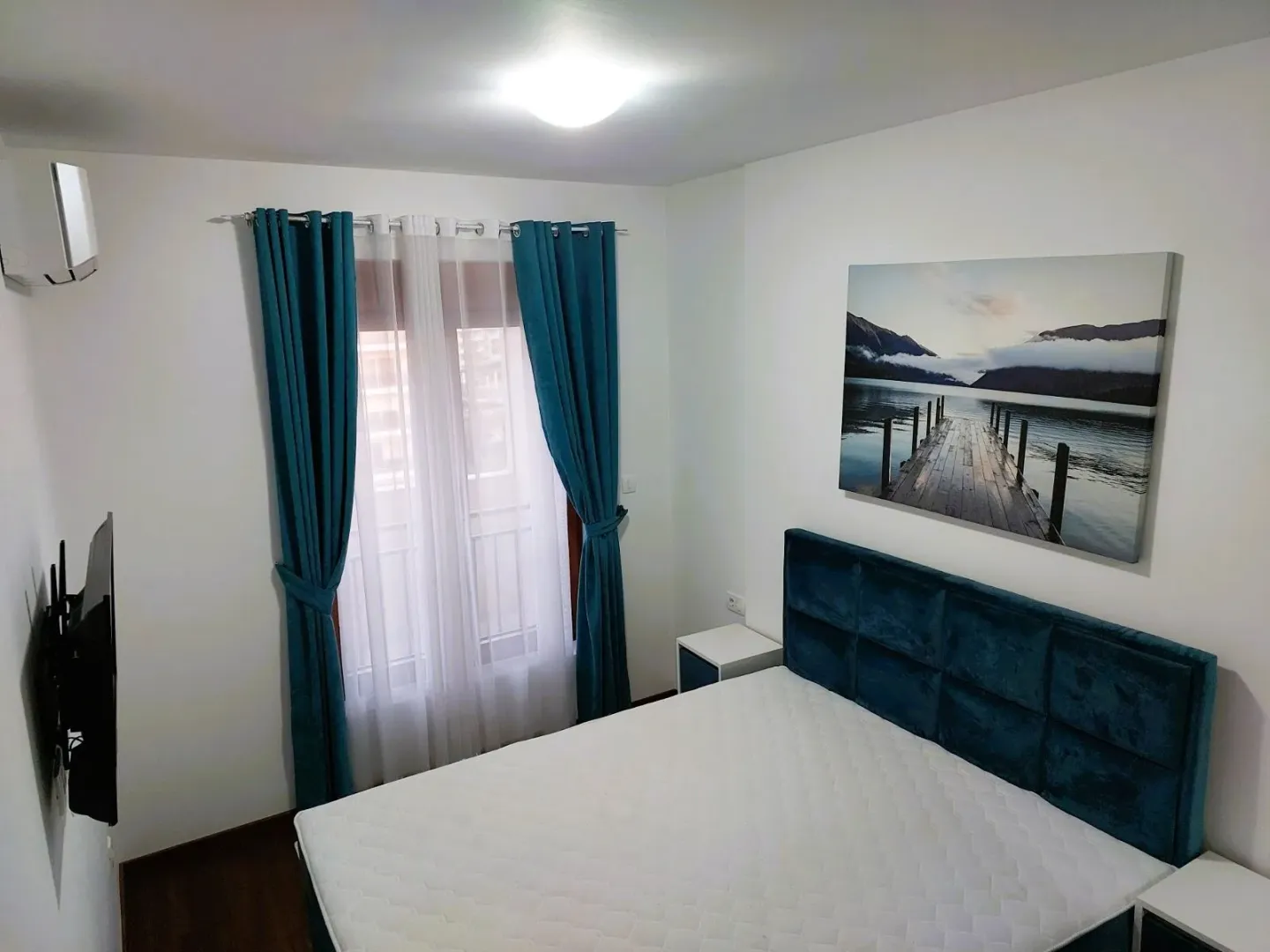 Furnished bedroom with a double bed and a window with blue curtains.