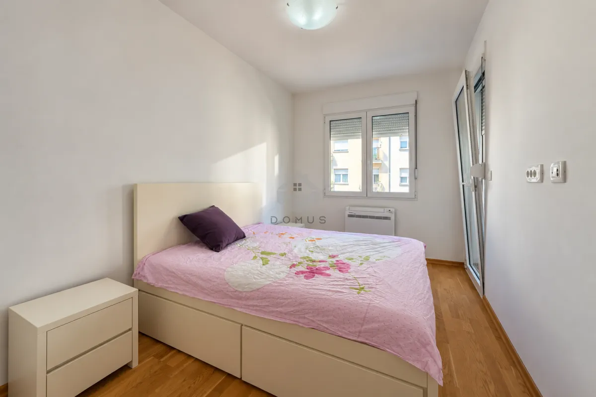Spavaća soba sa bračnim krevetom, noćnim ormarićem i izlazom na terasu.