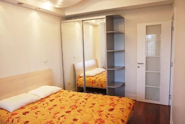 Namještena spavaća soba sa bračnim krevetom, velikim ormarom sa ogledalom i bijelim vratima.