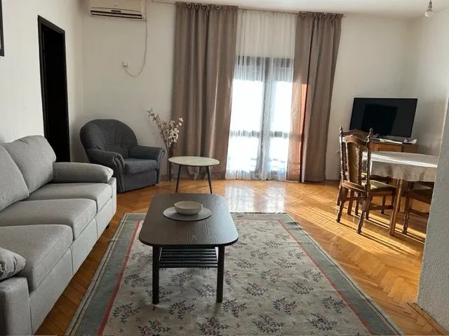 Living room with sofa, coffee table, dining table and parquet flooring.