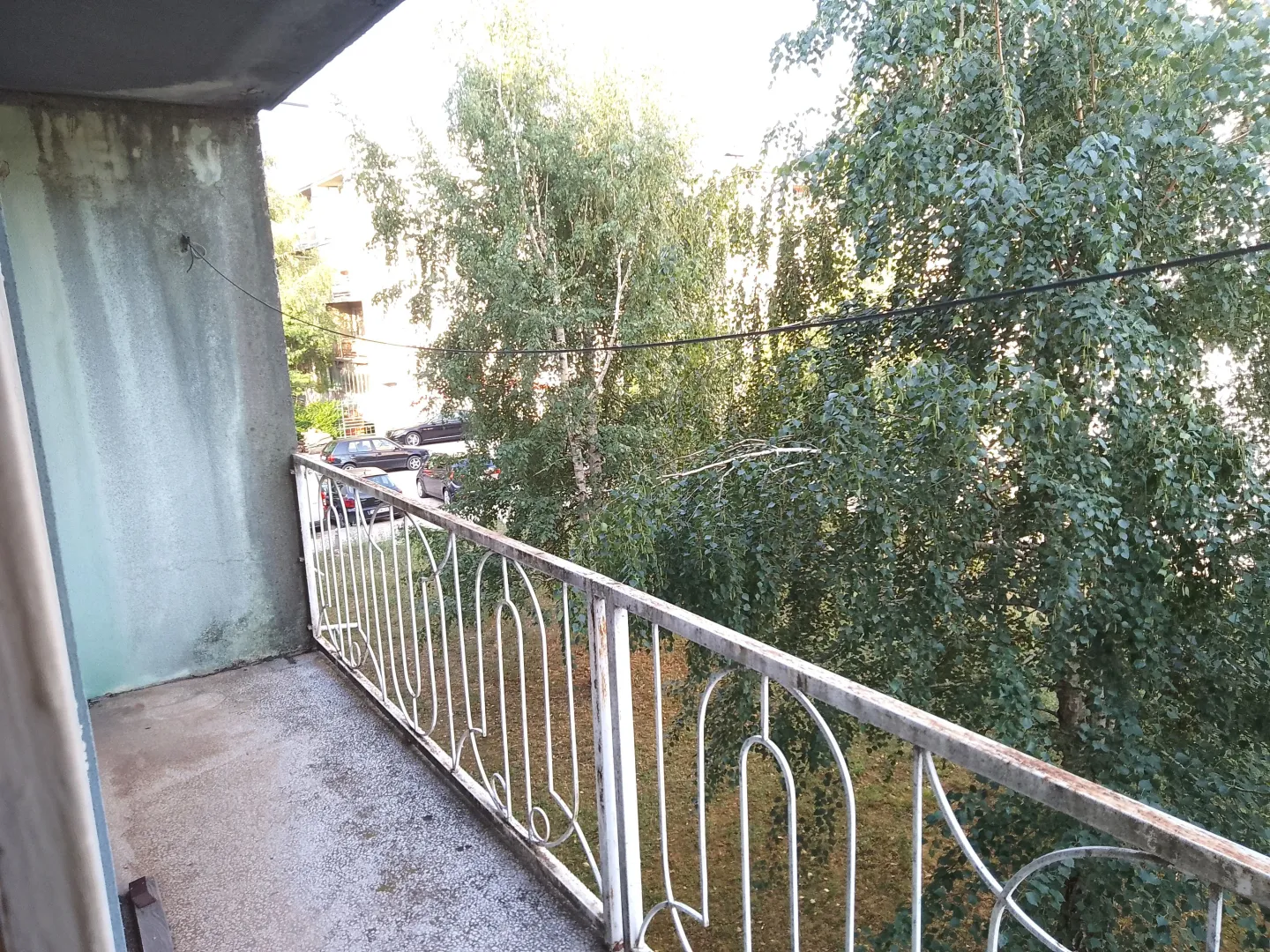 Manji balkon sa metalnom ogradom i pogledom na zelenilo.