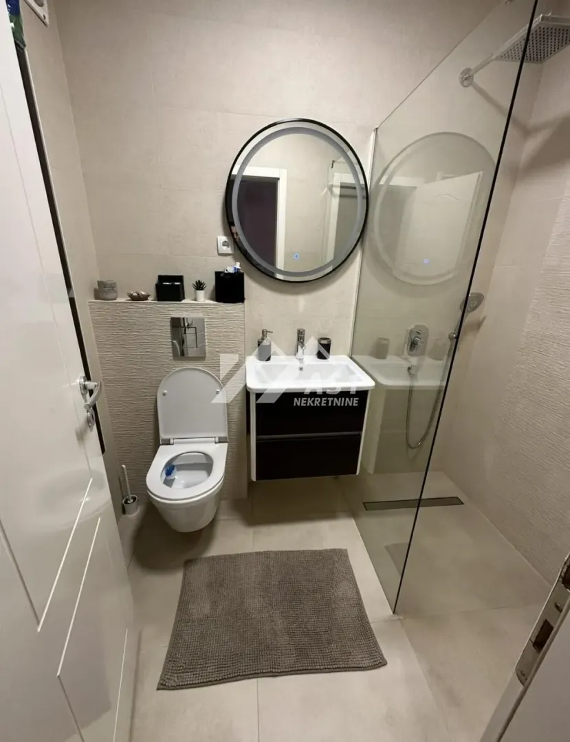 Moderno kupatilo sa tuš kabinom, konzolnom šoljom i umivaonikom.