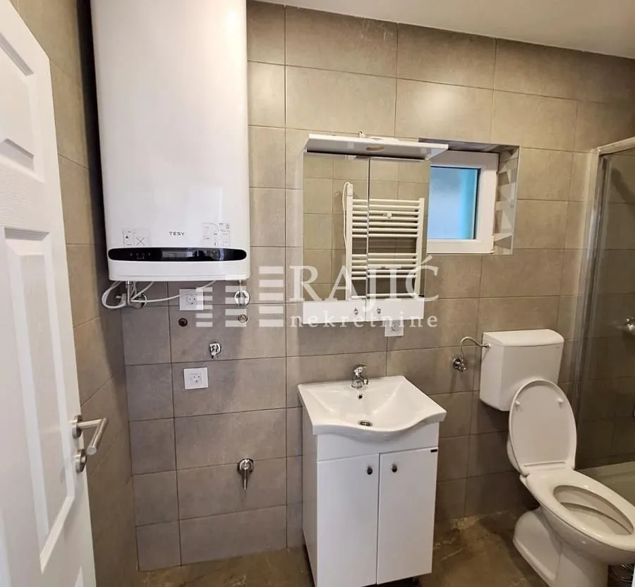 Manje kupatilo sa umivaonikom, WC šoljom, bojlerom i tuš kabinom.
