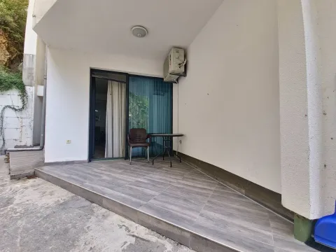 Covered terrace with ceramic tiles and a table with a chair in front of the apartment entrance. - image 8