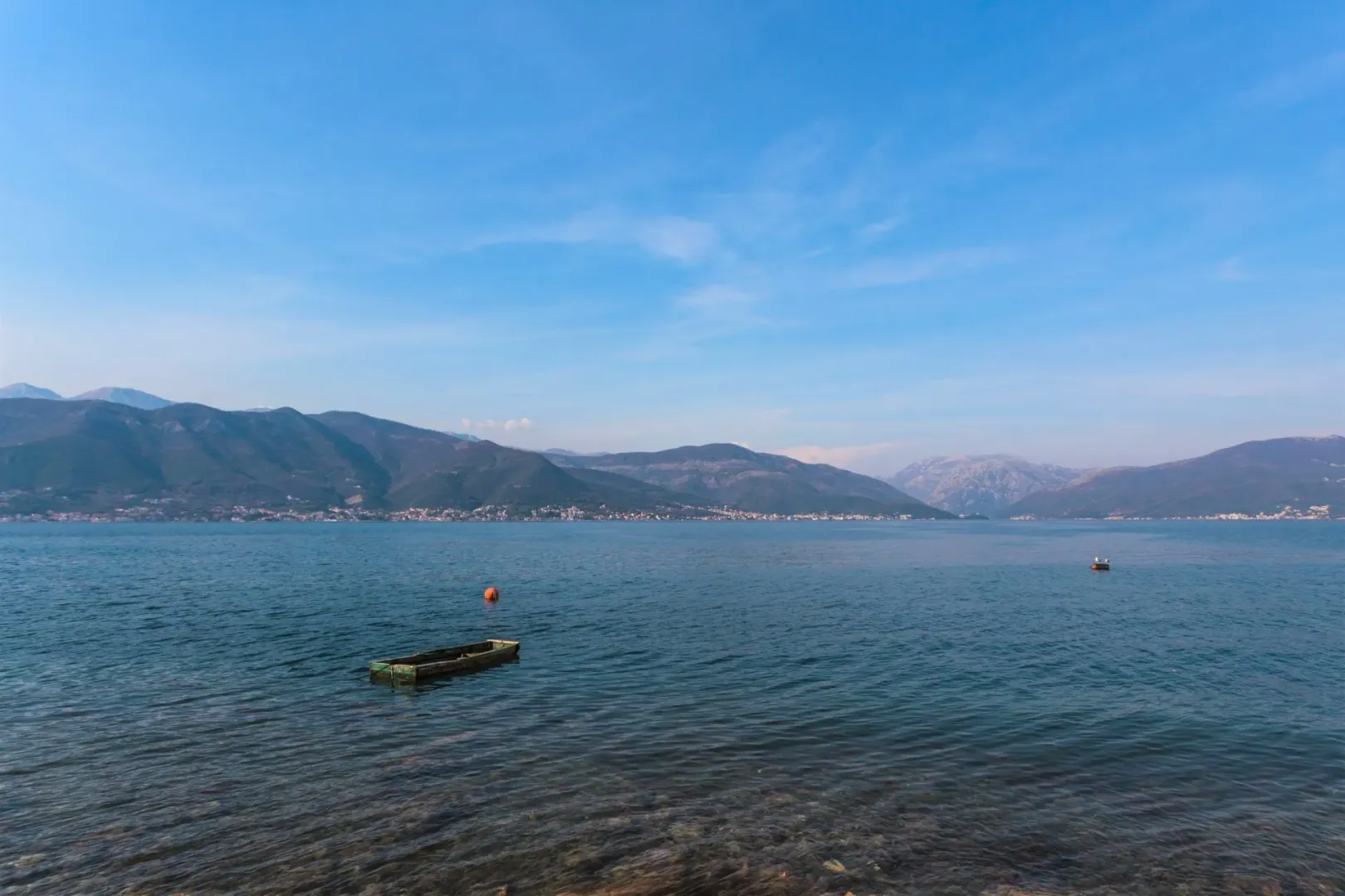 Pogled na more i planine u daljini sa malom barkom u vodi.