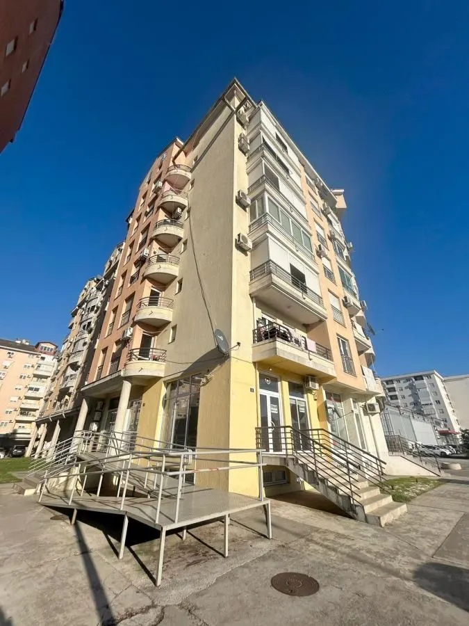 Pogled na spoljašnjost stambene zgrade sa stepeništem i rampom za pristup.