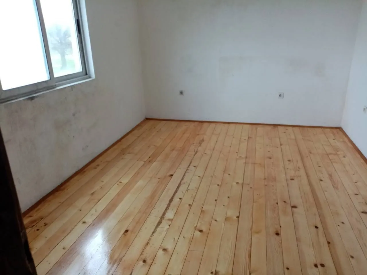 An empty room with wooden flooring and a window.
