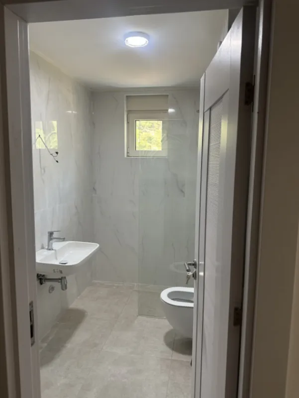 Pogled na kupatilo sa umivaonikom, WC šoljom i tuš kabinom kroz otvorena vrata.