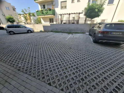 Otvoreni parking sa popločanim površinama i parkiranim automobilima ispred zgrade. - image 13