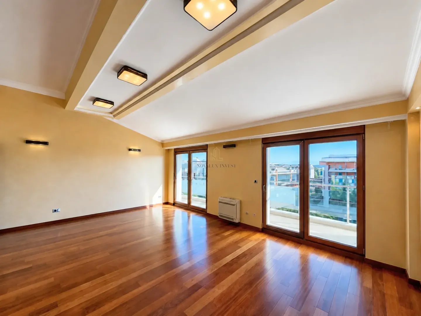 Empty living room with hardwood floor, dropped ceiling and balcony doors.