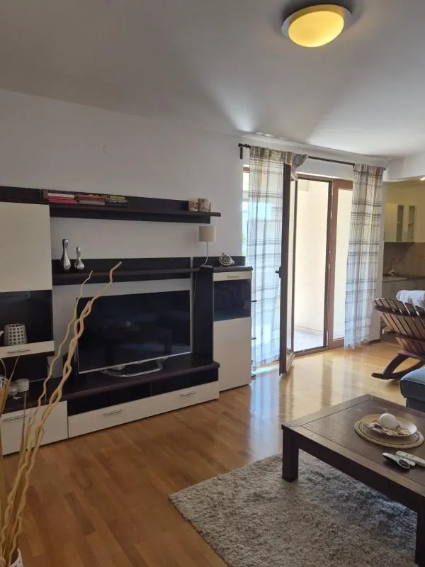 Dnevna soba sa garniturom, TV komodom i izlazom na terasu.
