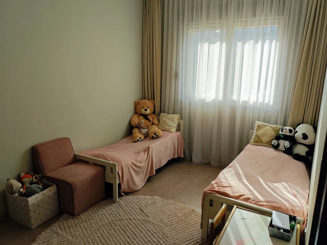 Dječija soba sa dva kreveta, foteljom i plišanim igračkama.