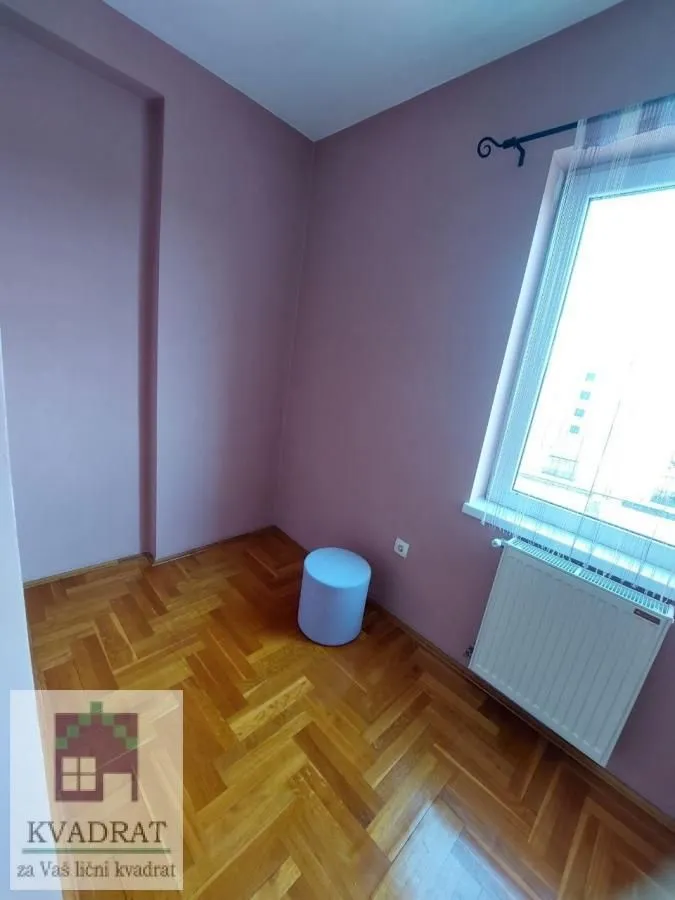 Empty room with pink walls, wooden parquet flooring, and a window.