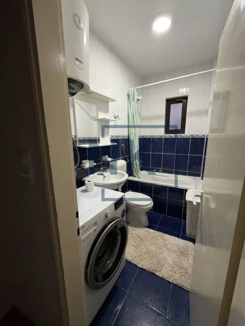 Small bathroom with blue tiles, bathtub, washbasin, washing machine, and water heater.