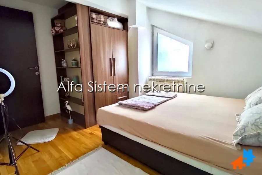 Nameštena spavaća soba sa bračnim krevetom i ugradnim ormanom pod kosim krovom.