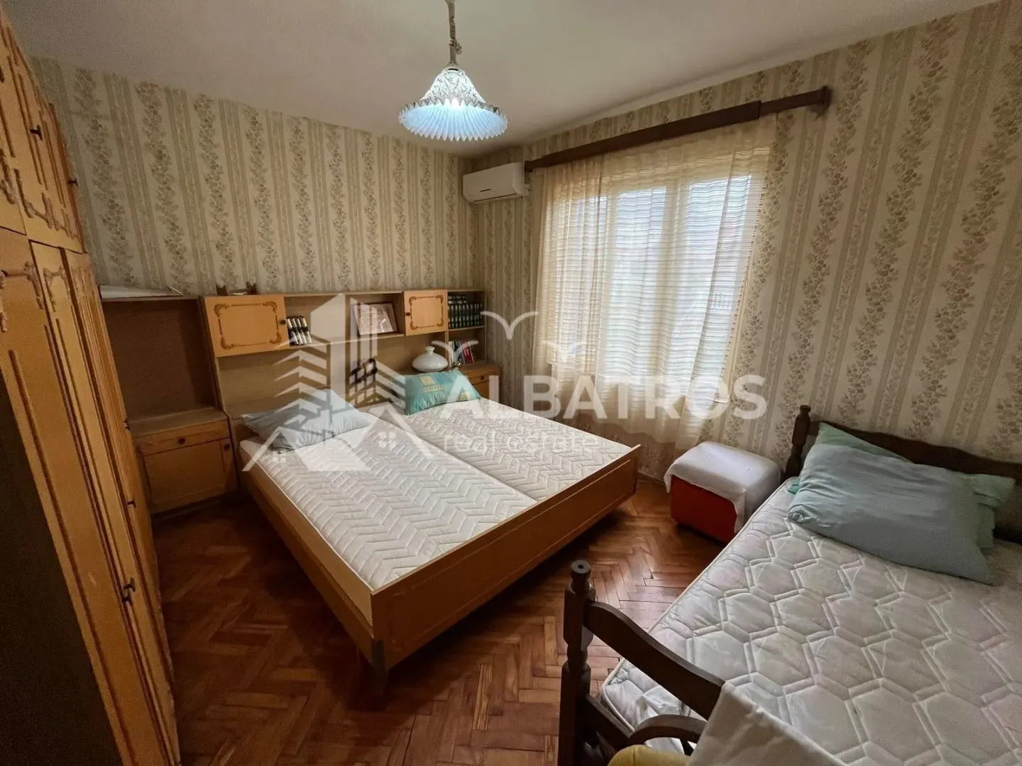 Namještena spavaća soba sa dva kreveta i drvenim ormarima.