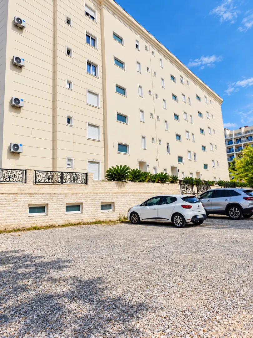 Spoljašnji izgled stambene zgrade sa parkingom.