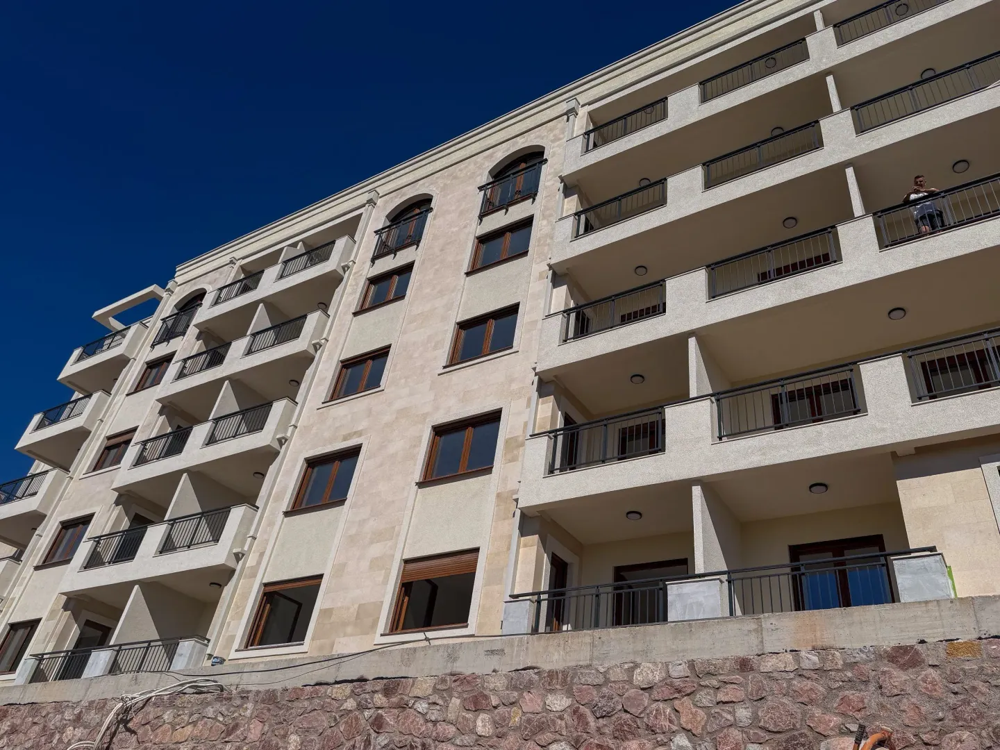 Pogled na spoljašnjost moderne stambene zgrade sa terasama i kamenom bazom.