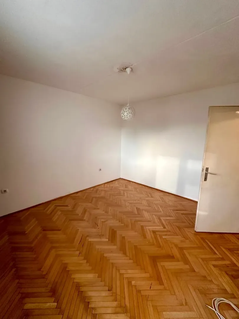 Prazna soba sa parketom i bijelim zidovima.