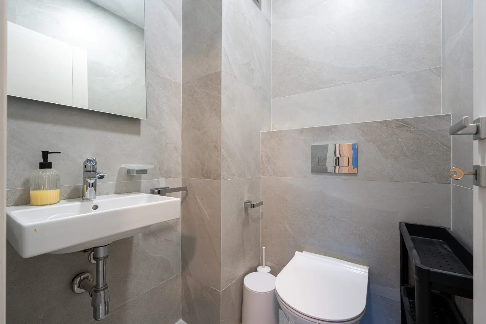 Modernly equipped bathroom with a washbasin and toilet, tiled in grey.