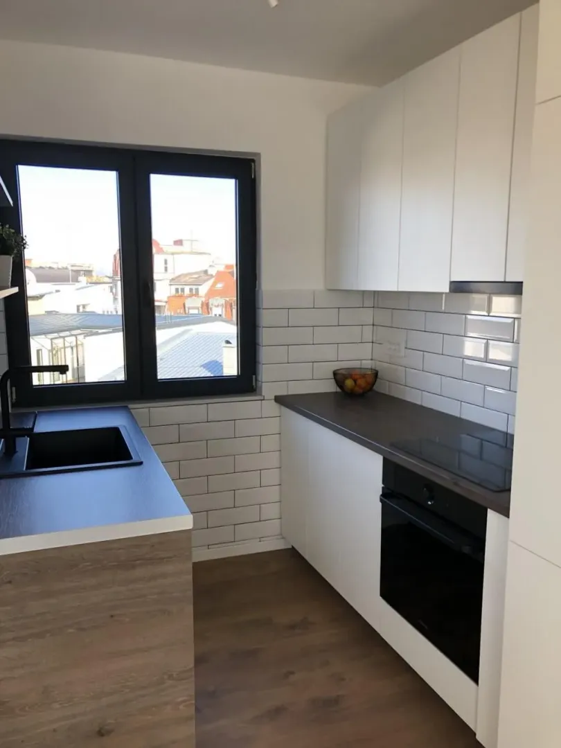 Modern kitchen with white cabinetry, dark countertop and a window.