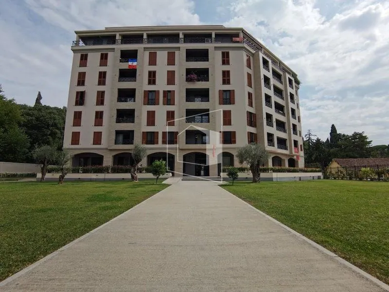 Spoljašnji izgled višespratne stambene zgrade sa uređenim travnjakom i stazom u dvorištu.
