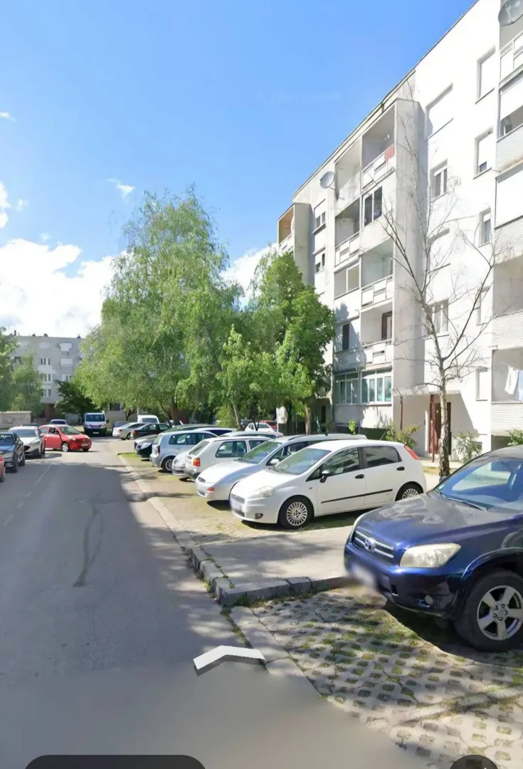 Pogled na stambenu zgradu i parking ispred ulaza.