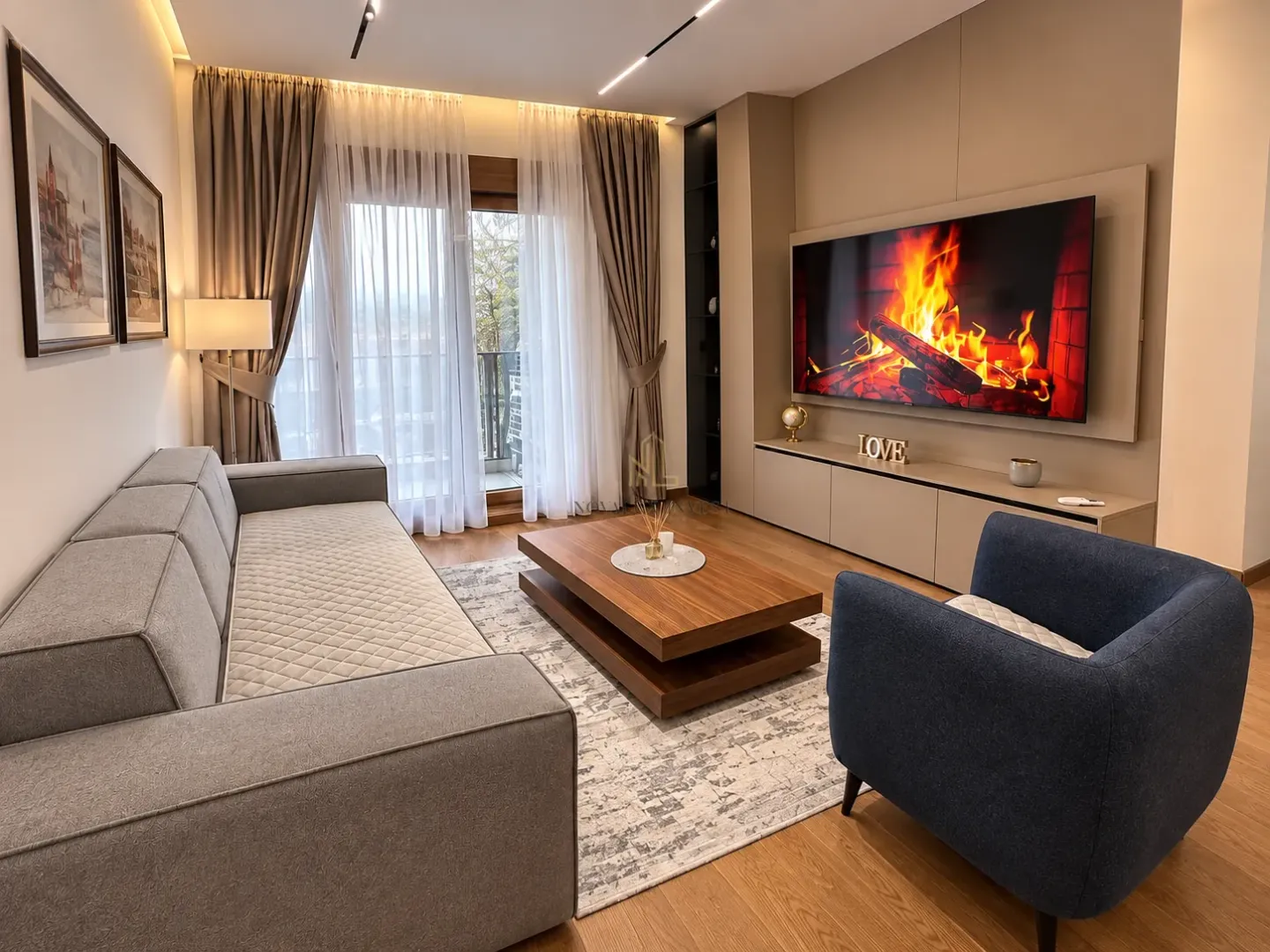 Living room furnished with a modern sofa, wooden coffee table, and a large TV.