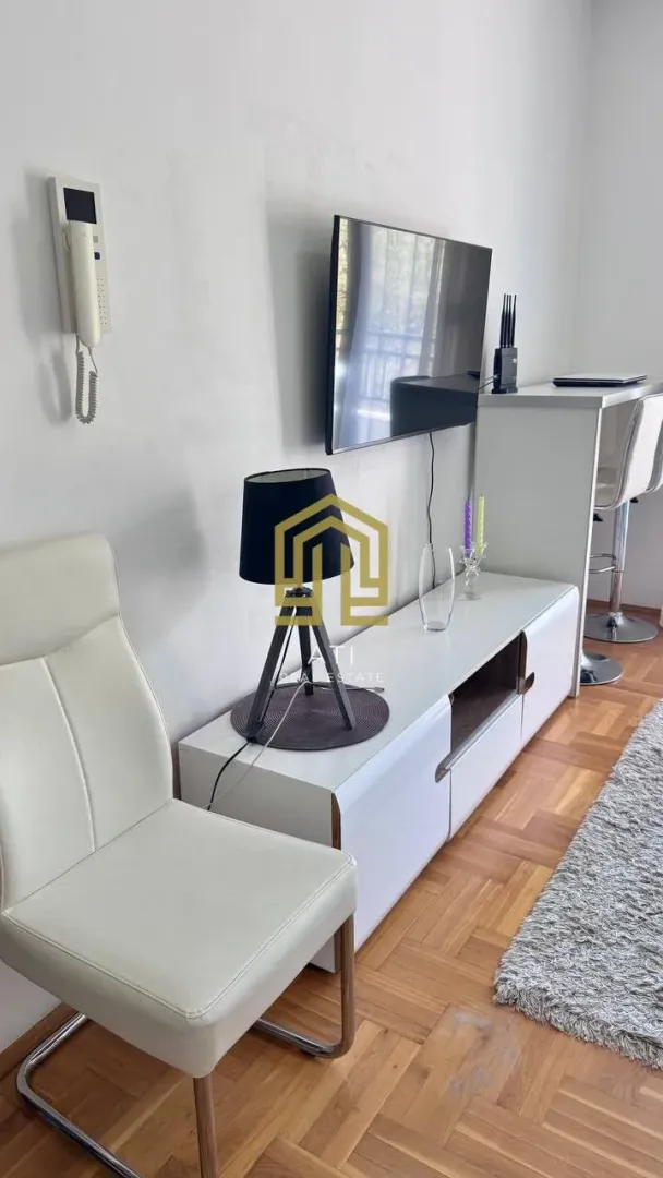 Dnevna soba sa bijelim namještajem, televizorom i trpezarijskim stolom.