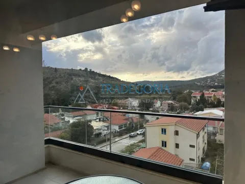 Natkrivena terasa sa staklenom ogradom i pogledom na naselje i brda. - image 18