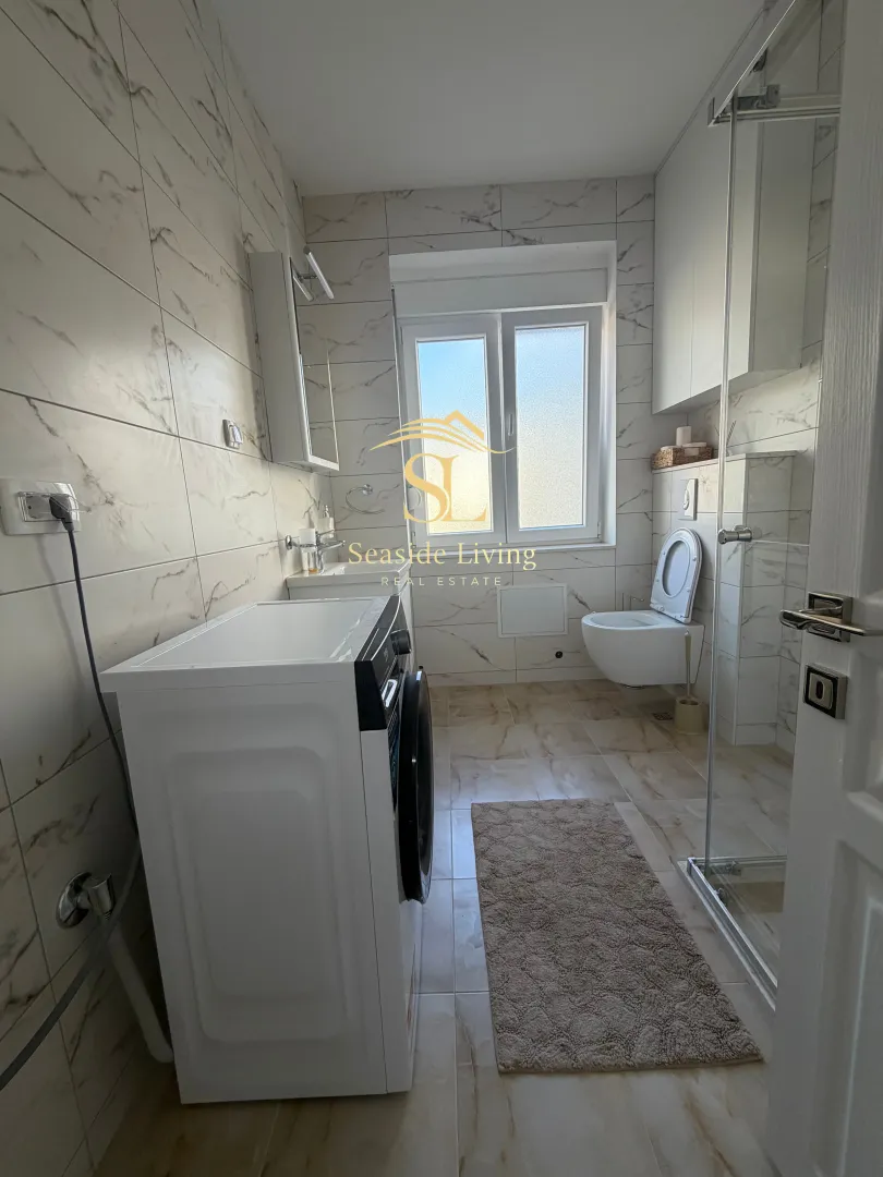 Moderne kupatilo sa tuš kabinom, veš mašinom i WC šoljom.