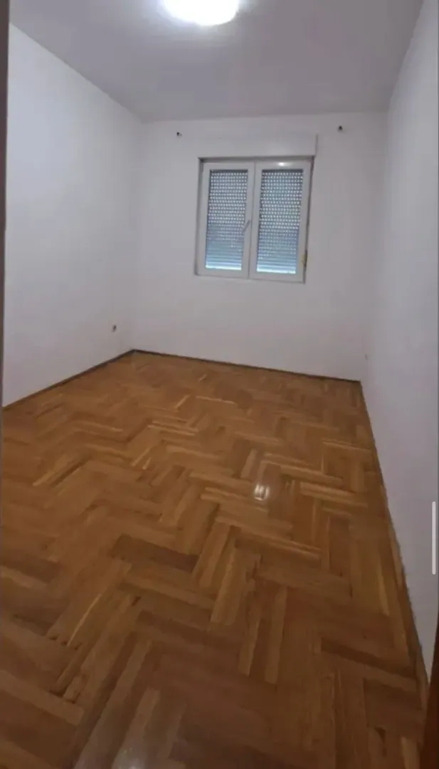 Prazna prostorija sa bijelim zidovima i drvenim parketom.