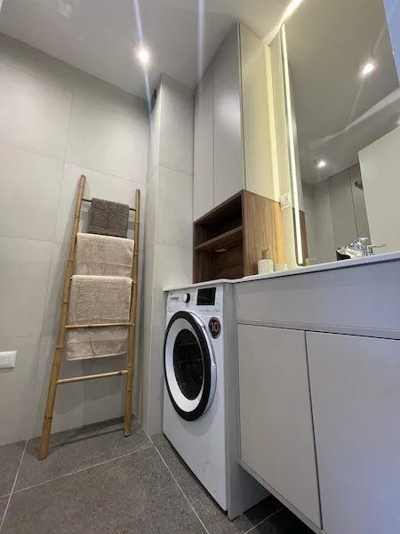 Modern bathroom with a washing machine, vanity unit, and a decorative wooden towel rack.
