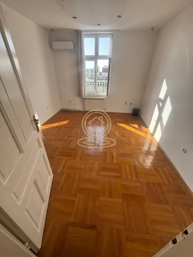Empty room with wooden parquet flooring and a window.