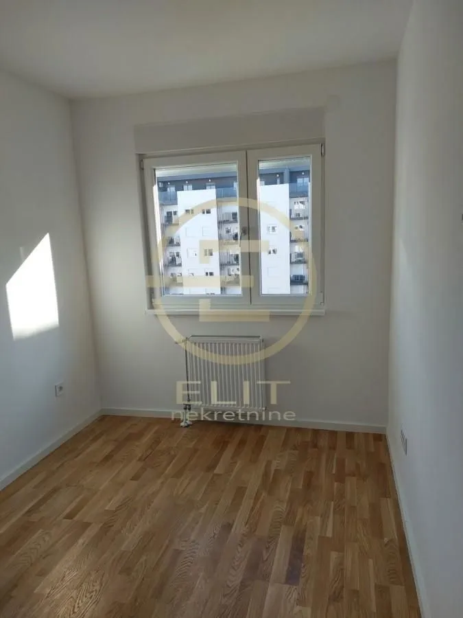 Prazna soba sa parketom i prozorom koji gleda na susednu zgradu.