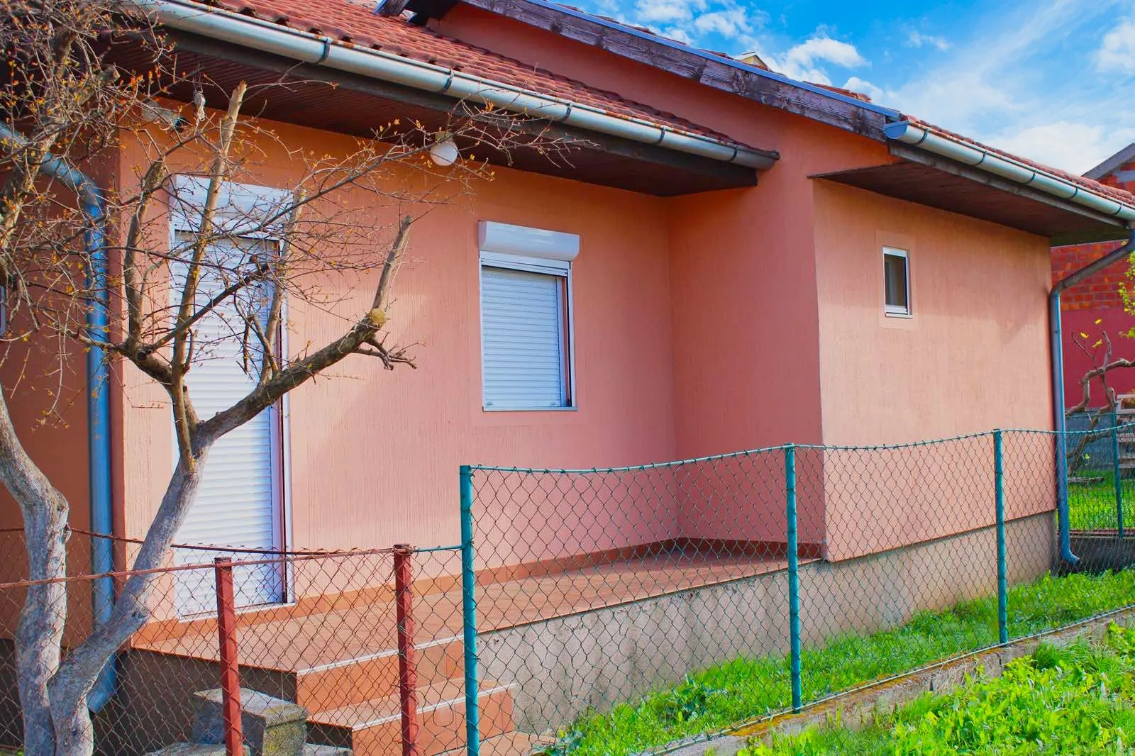 Spoljašnji pogled na prizemnu kuću sa fasadom i ograđenim dvorištem.