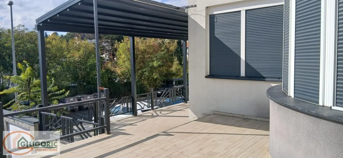 Prostrana natkrivena terasa sa popločanim podom i metalnom ogradom.