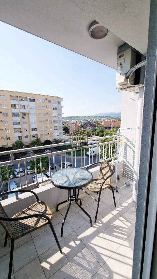 Small furnished balcony with a table, chairs, and a view of surrounding buildings and neighborhood.