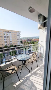 Small furnished balcony with a table, chairs, and a view of surrounding buildings and neighborhood. - image 3