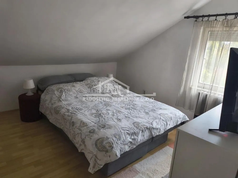 Potkrovna spavaća soba sa bračnim krevetom i kosim plafonom.