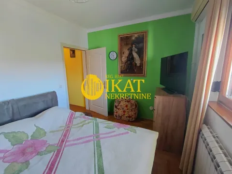 Nameštena spavaća soba sa bračnim krevetom, televizorom i zelenim zidom. - image 9