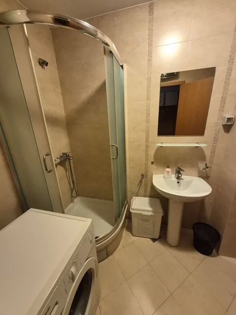 Compact bathroom equipped with a shower cabin, sink, and washing machine.