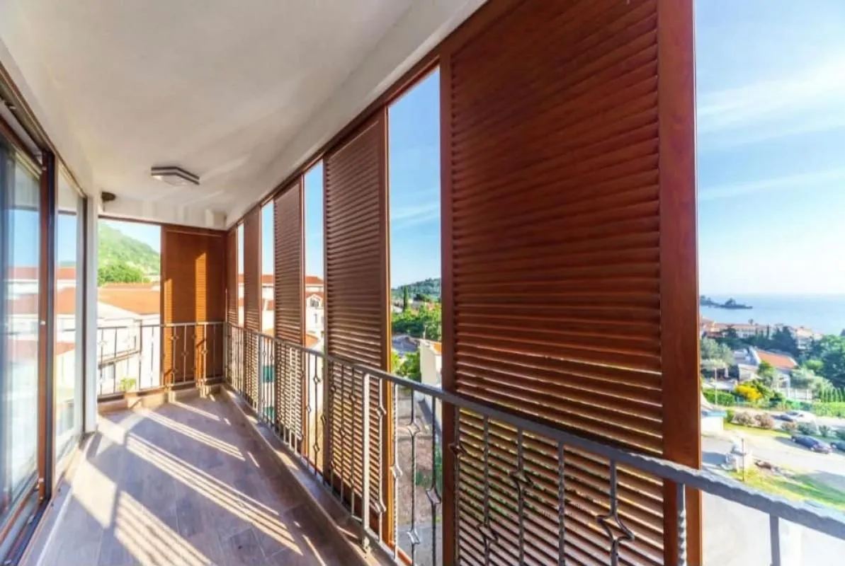 Natkriveni balkon sa drvenim žaluzinama i pogledom na more.