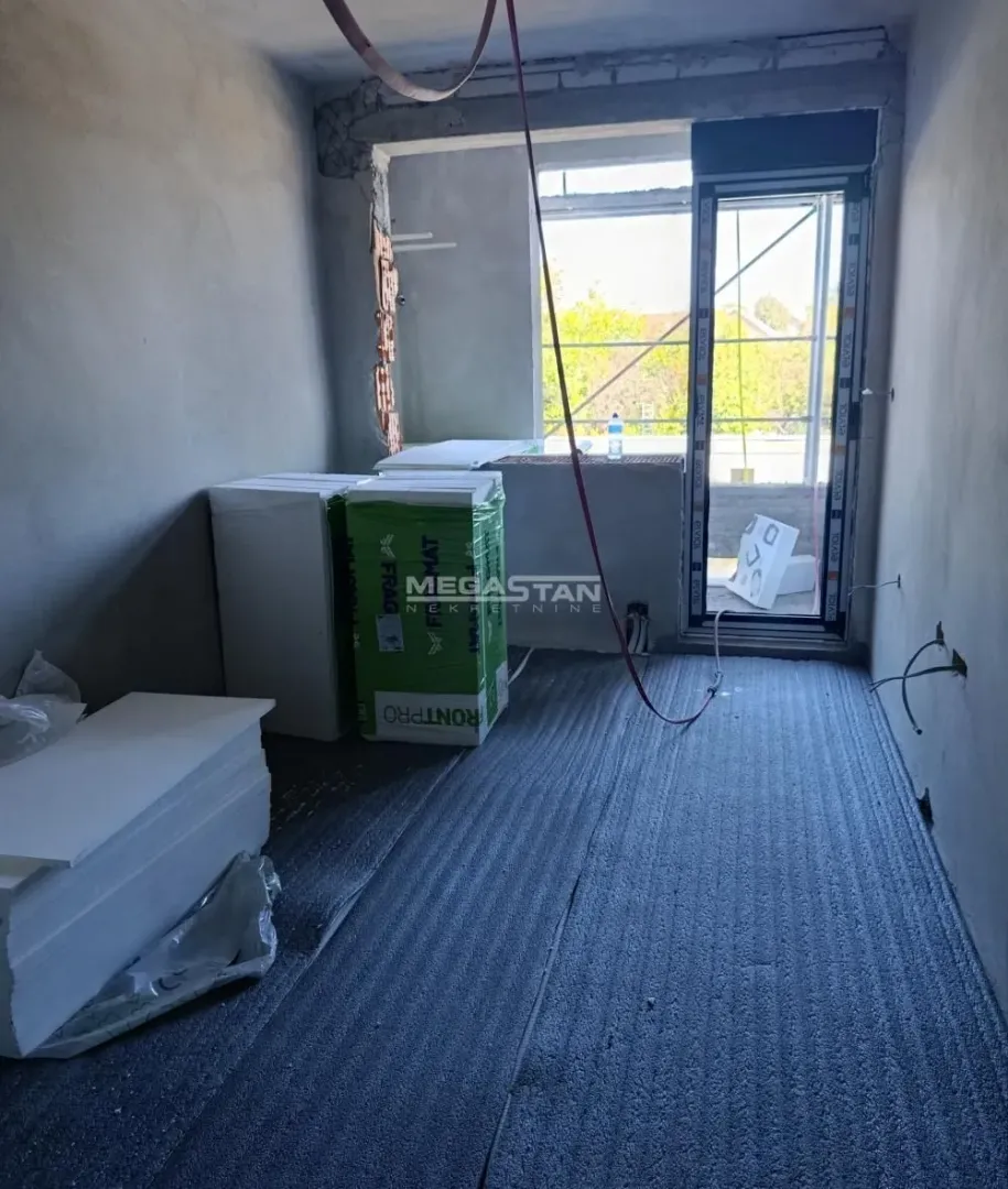 Prazna prostorija u toku renoviranja sa građevinskim materijalom i izlazom na terasu.
