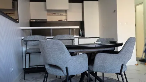 Modern dining area with a table and grey-and-white kitchen elements in the background. - image 3