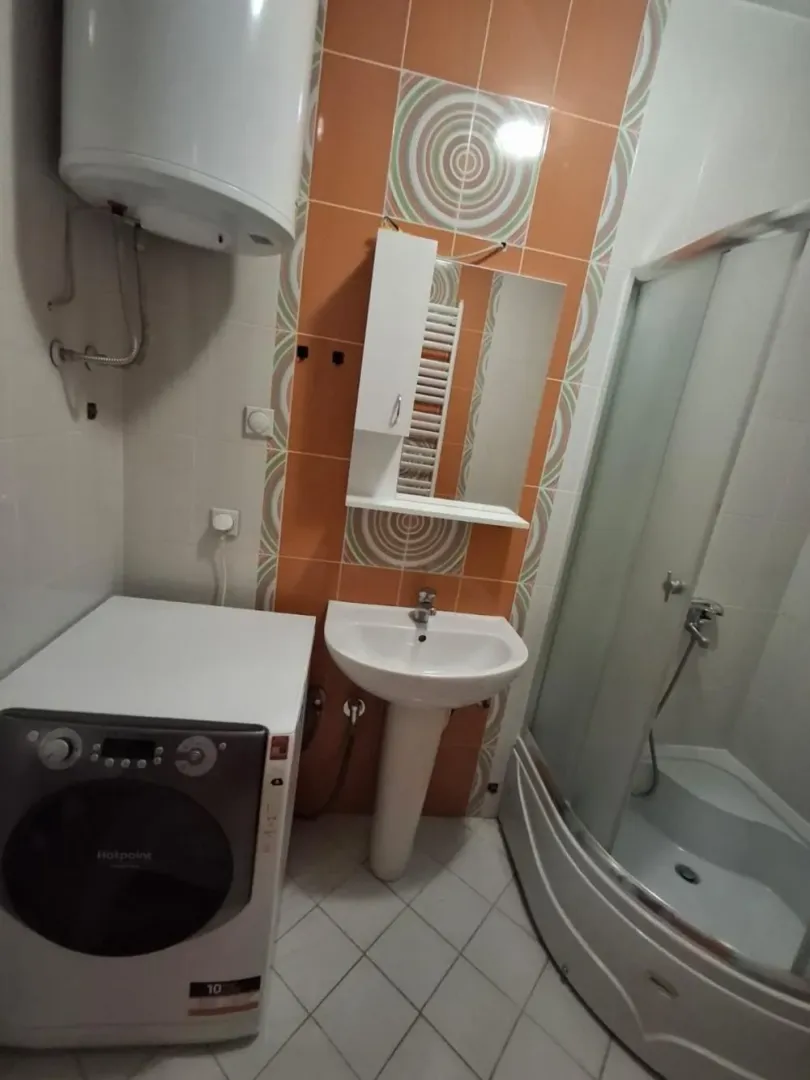 Bathroom with a shower cabin, washbasin, water heater, and washing machine.