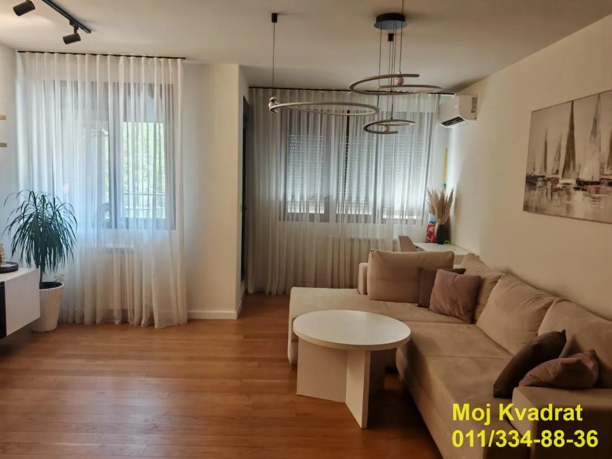 Dnevna soba sa ugaonom garniturom, stočićem i velikim prozorima.