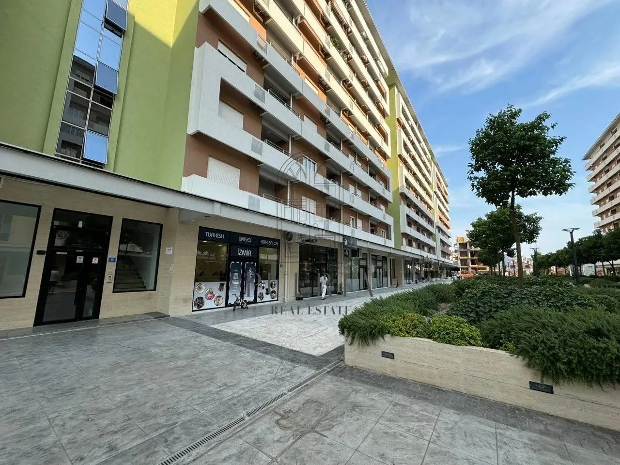 Exterior of a residential building with ground-floor commercial spaces and a paved walkway.