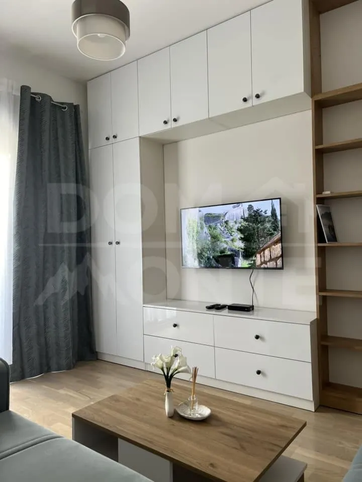 Dnevna soba sa bijelim ormarima, TV-om i drvenim stočićem.