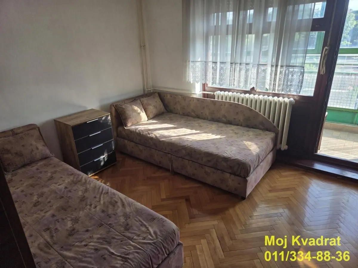 Nameštena spavaća soba sa dva kreveta i izlazom na terasu.